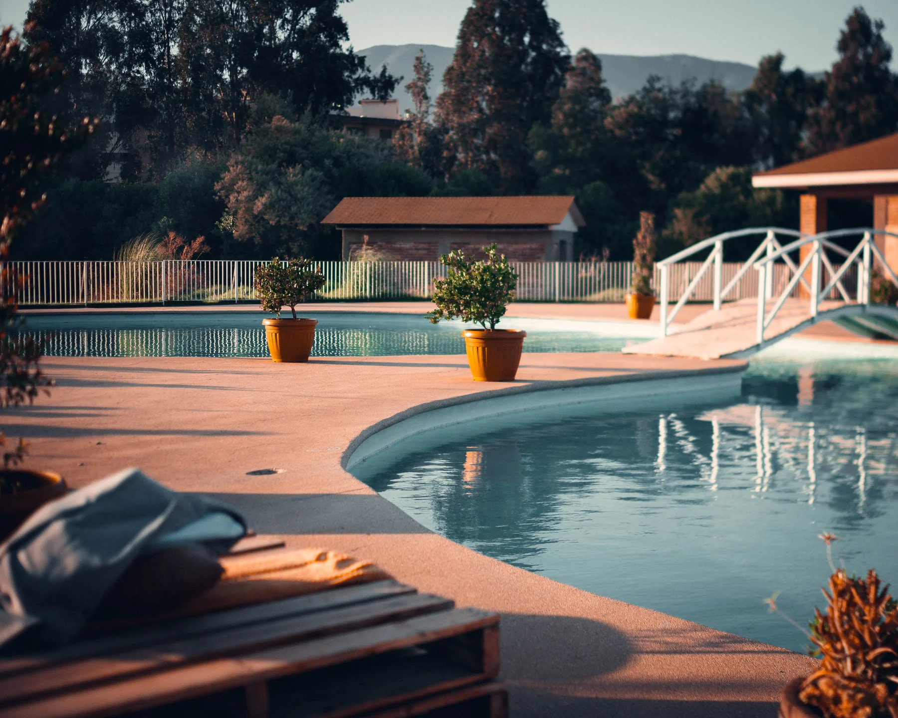 Piscina exterior con pasarela, vegetación y zona de descanso